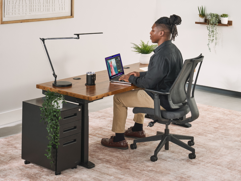 Man seated upright at a standing desk with his feet flat and knees bent at 90 degrees.