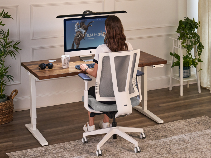 Woman seated in a mesh office chair with the backrest supporting her back at a standing desk.
