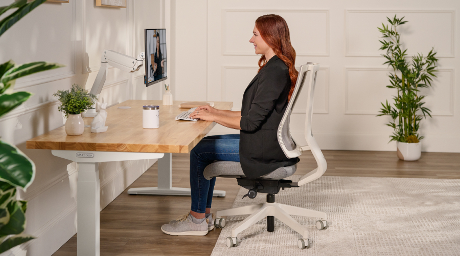 Woman seated at a standing desk with her feet flat and thighs level in an office chair.