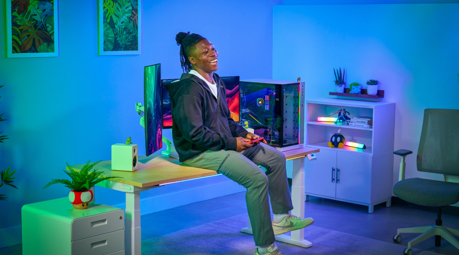 Man sitting on an UPLIFT 4-Leg Standing Desk alongside heavy desk equipment.