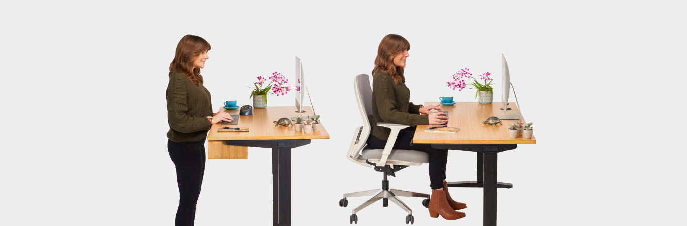 Someone working at a height adjustable desk while standing and another while sitting
