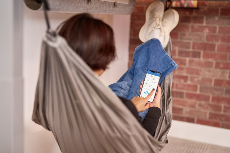 A person reclines in an UPLIFT Under Desk Hammock while raising the desk with the app.
