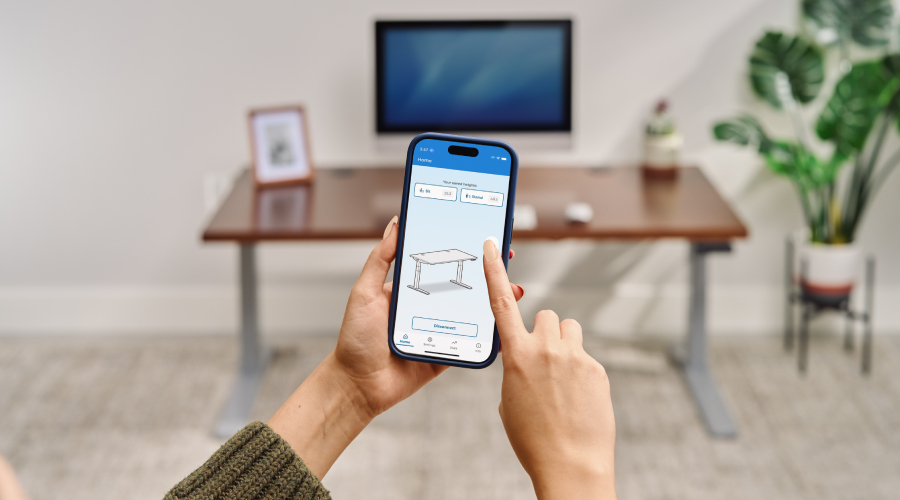 A person adjusts an UPLIFT Standing Desk using the UPLIFT Desk App on a phone.