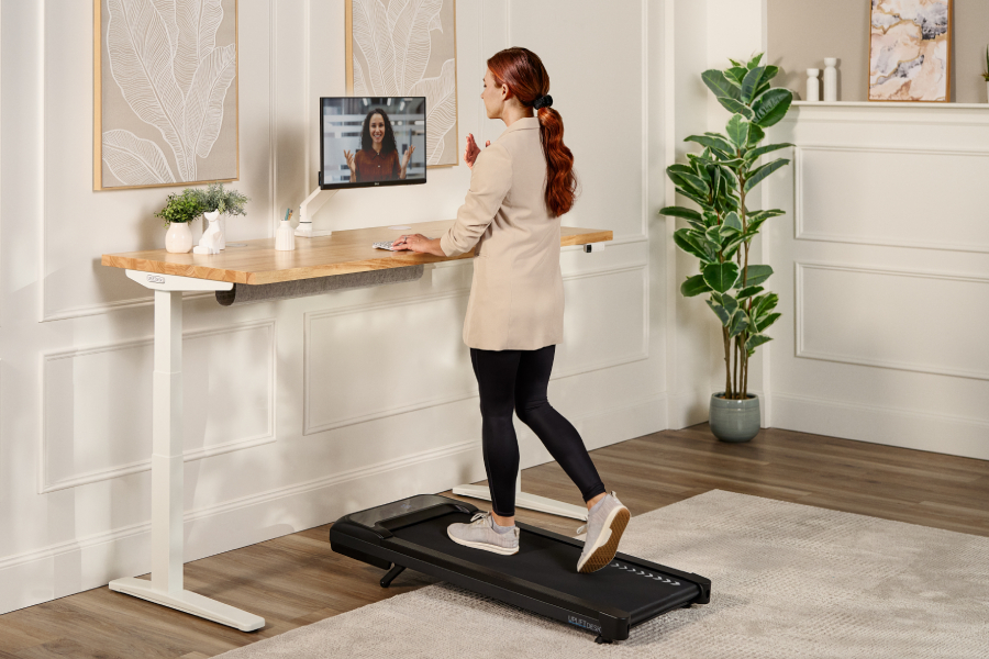 Woman walking on walking pad by UPLIFT Desk while working at a standing desk.