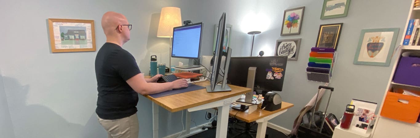 A member of the Out Youth team stands at a donated UPLIFT Standing Desk with another donated UPLIFT desk in the background
