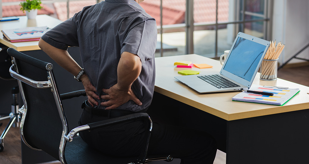 Person stretching lower back while seated at a desk that's too small for proper ergonomic support and workspace needs.