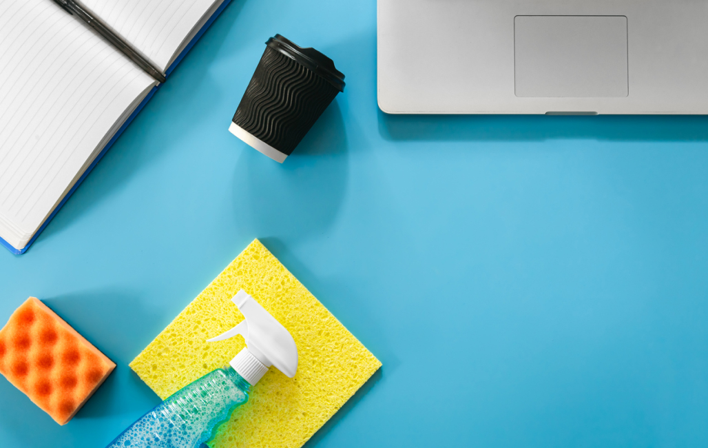 Overhead view of a desk with cleaning supplies and a coffee cup on its side.
