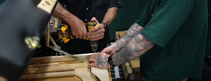 Detailed view of hands using a power drill to assemble a wooden desk frame.