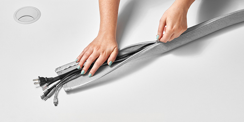 Person organizing their cables with a zip sleeve for their standing desk cable management.