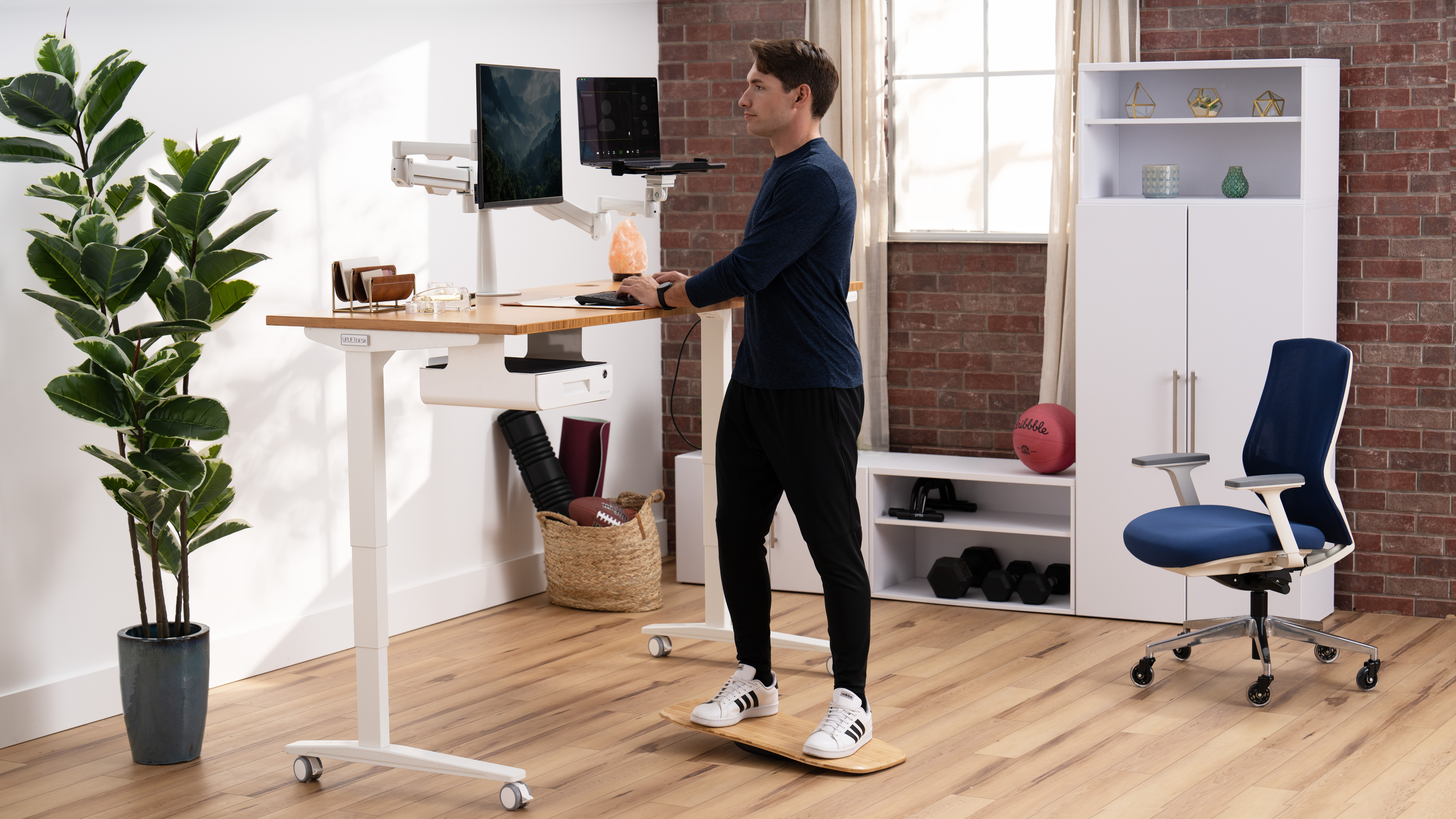 Man working at a standing desk by UPLIFT Desk featuring various desk accessories and storage.