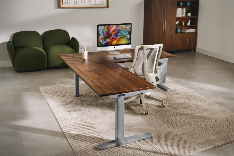 The UPLIFT L-Shaped Standing Desk shown in the foreground with a laminate desktop and matching frame