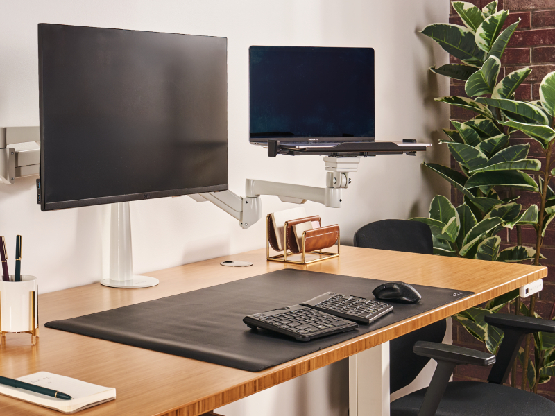 An articulating monitor arm and laptop mount positioning displays at eye level on a standing desk