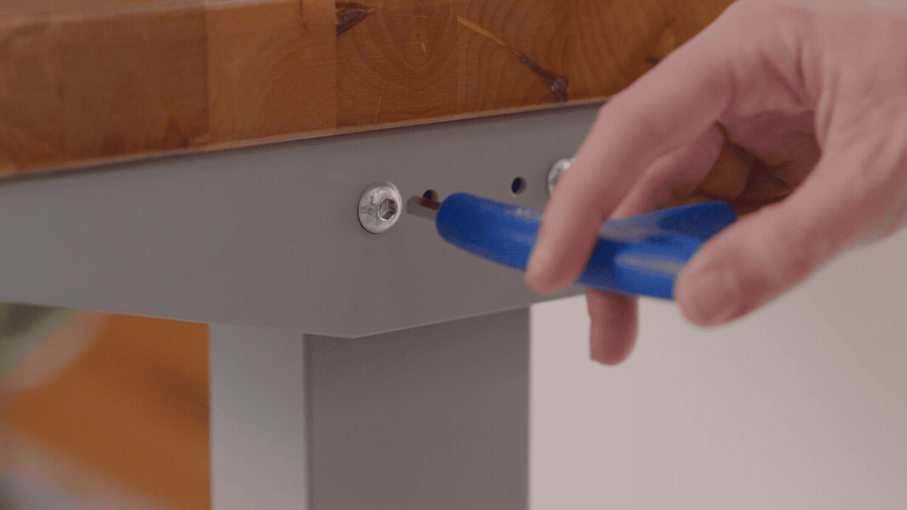 Person screwing in desk frame fastenings with the included Allen wrench tool.